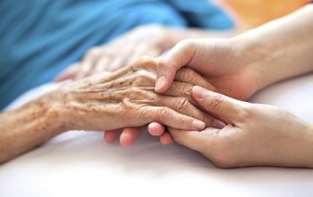 Woman holding senior woman's hand on bed